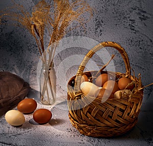 Easter composition. Basket with eggs, several eggs bouquet of dried flowers on a gray background