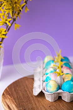 Easter composition with colorful eggs in a basket, spring yellow flowers on a purple background. Banner. Copy space.