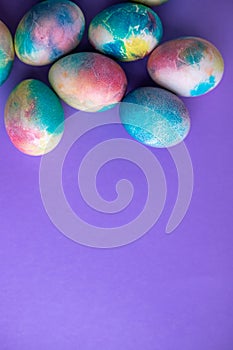 Easter composition with colorful eggs in shopping cart, wooden bunny and spring flowers on purple background. Easter