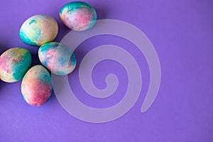 Easter composition with colorful eggs in shopping cart, wooden bunny and spring flowers on purple background. Easter