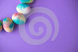 Easter composition with colorful eggs in shopping cart, wooden bunny and spring flowers on purple background. Easter