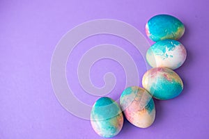 Easter composition with colorful eggs in shopping cart, wooden bunny and spring flowers on purple background. Easter