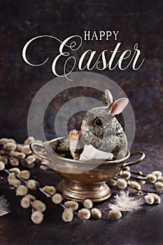 Easter composition with a cute bunny figurine and catkin twigs on grunge background with greeting text