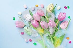 Easter composition with eggs, spring flowers, feathers and colorful candy on blue table top view.