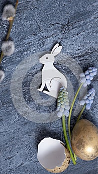 Easter composition with flowers, white wooden rabbit and eggs flat lay, top view on cement background.