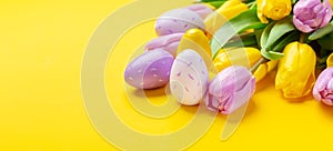 Easter composition. Multicolored easter eggs and tulips on yellow background. Easter concept. Copy space