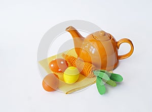 Easter composition. Orange teapot with knitted eggs and a carrot. White background.