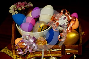Easter composition with painted chicken eggs in different colors in a white plate on a wooden stand with a red box of chocolates,