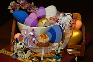 Easter composition with painted chicken eggs in different colors in a white plate on a wooden stand with a red box of chocolates,
