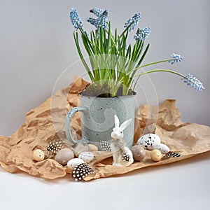 Easter composition with white rabbit, eggs, feathers and light blue muscari flowers in cup. Easter still life