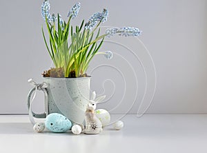 Easter composition with white rabbit, eggs and light blue muscari flowers in cup. Easter still life