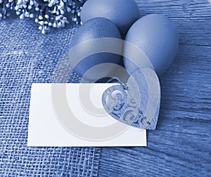 Easter composition on wooden background.  Eggs, empty card with decor heart on sackcloth. Toned  blue image.