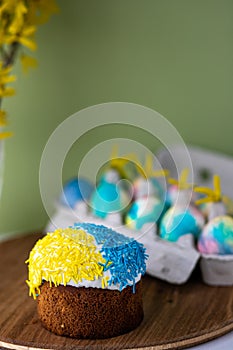 Easter composition with yellow-blue Easter cakes, sprinkles, Easter multi-colored eggs. wooden stand and spring flowers