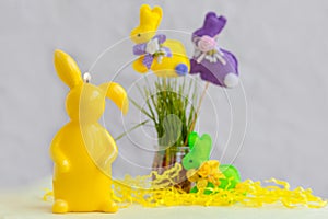 Easter composition with yellow candle, toy bunnies, green grass. Festive table decoration.