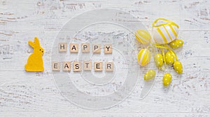 Easter concept banner. Yellow rabbit, eggs and wooden letters Happy Easter on a white background. Minimalism.