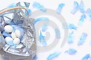 Easter concept. basket decorated with silver paper, white eggs and blue feathers.