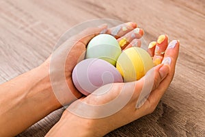 Easter concept. closeup beautiful woman hands holding three eggs colored in tender pastel colors yellow, mint and purple over