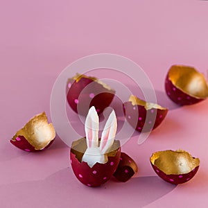 Easter concept. Colored eggs on pink background, Easter Bunny hiding inside. Red with pink polka dots, gold inside