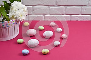 Easter concept. Easter multi-colored eggs near a basket with white flowers on a red table on a background of a white