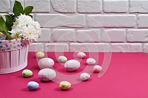 Easter concept. Easter multi-colored eggs near a basket with white flowers on a red table on a background of a white