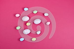 Easter concept. Easter multi-colored eggs near a basket with white flowers on a red table on a background of a white