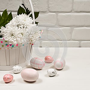 Easter concept. Easter pink eggs near a basket with white flowers on a wooden table on a background of a white wall
