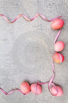 Easter concept pink rosy eggs with satin polka dot ribbons in sunny rays. On stone background. Frame
