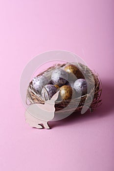 Easter concept - rabbit in a nest with chocolate eggs against pink background