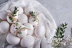 Easter concept. White chicken eggs on white fabric. Decorated with eucalyptus leaves. Top view