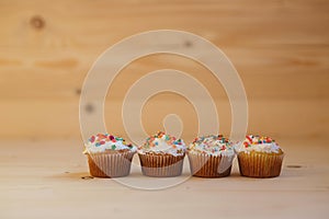 Easter cupcakes with cream and small confetti on a wooden table.