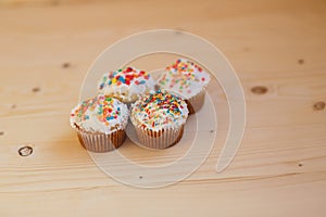 Easter cupcakes with cream and small confetti on a wooden table.