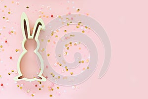 Easter decoration with bunny and confetti on pink background.