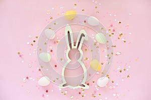 Easter decoration with bunny eggs and confetti on pink background.