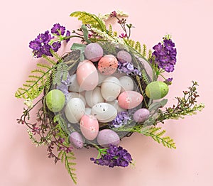 Easter decoration, egg nest on pink background. Festive flower wreath full of pastel color egg