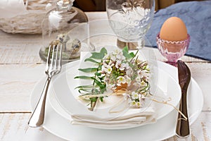 Easter decoration table setting, white plates, napkin, flowers in eggshell, green sprigs, outdoors