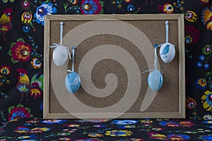 Easter decoration with white and blue eggs on painted textile background with corkboard.