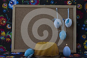 Easter decoration with white and blue eggs on painted textile background with corkboard.