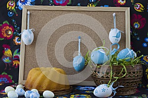 Easter decoration with white and blue eggs on painted textile background with corkboard.