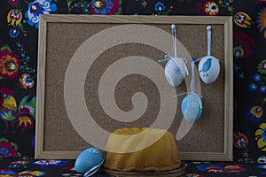 Easter decoration with white and blue eggs on painted textile background with corkboard.