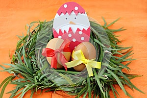 Easter decoration: yellow eggs and hand made hatched chicken in eggshell in green grass twigs nest on orange background