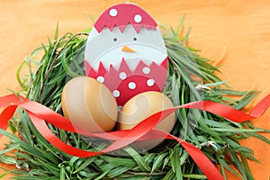 Easter decoration: yellow eggs and hand made hatched chicken in eggshell in green grass twigs nest on orange background