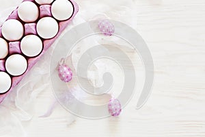 Easter decoration â€“ white eggs and Milticolor bird feathers. Top view, close up, flat lay on white wooden background