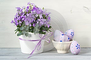 Easter decorations with bowl full of easter eggs and a pot of spring purple flowers on a white wooden background