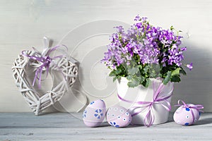 Easter decorations with easter eggs, a pot of spring purple flowers and heart on a white wooden background