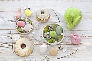 Easter decorations with eggs, moss and ceramic figurines on white wooden table