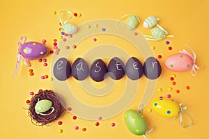 Easter decorations on yellow background. Papier-mache eggs painted with chalkboard paint. View from above.