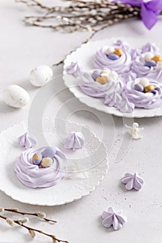 Easter dessert Mini Pavlova Birds Nests with colorful eggs candy on a light background. Meringue Cookies. Festive Food recipe.