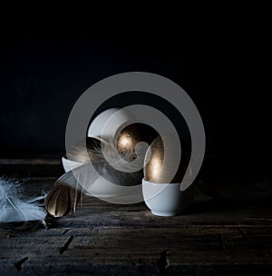 Easter. Easter night. Golden and White eggs, feathers on a wooden table. Vintage. Dark background