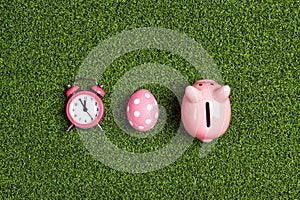 Easter egg, alarm clock and piggy bank on a green grass background