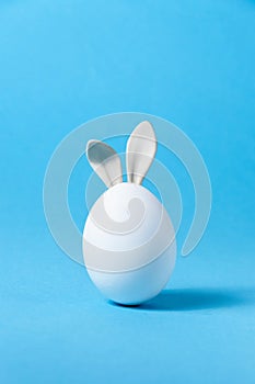 Easter Egg with Bunny Ears on Blue Background. Creative Greeting Card. Minimalism Concept. Copy Space